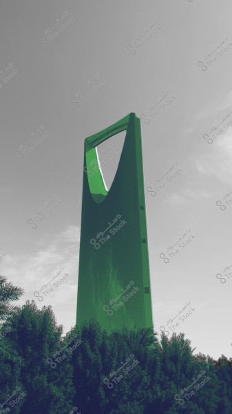 An image of the iconic Kingdom Tower in Riyadh, Saudi Arabia, displayed in a striking green color. The tower is tall with a distinctive architectural design featuring a large opening at the top. Dense green trees are visible in the foreground, and the sky in the background has light clouds.