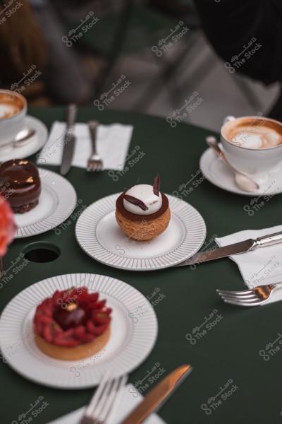 كعكات وحلويات متنوعة موضوعة على أطباق بجانب فناجين قهوة على طاولة خضراء.