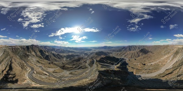 Stunning panoramic view of a winding mountain road in a hilly terrain under a blue sky and bright sun.