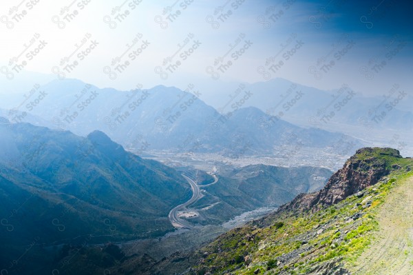 A snapshot of a series of towering rocky mountains and paved roads extending in the Al Hada Mountains in Taif, showing a cloudy sky during the day, mountain heights, Taif Mountains, mountain range