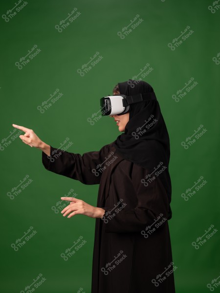 سيدة ترتدي نظارات الواقع الافتراضي وتستخدم يدها للتفاعل, بخلفية خضراء.