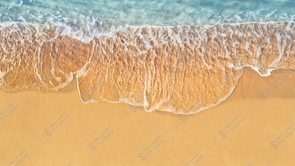 A top-down view of ocean waves gently lapping against the golden sandy beach. The blue water meets the sand in a soothing and repetitive pattern.