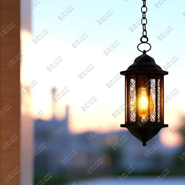 A traditional lantern hanging from a chain, illuminated in the dusk against a sunset background. The lantern features an intricate design and is made of metal, casting warm and vibrant colors in the dim light.