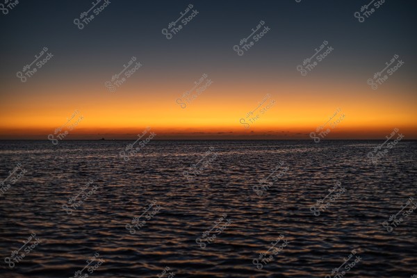 A view of the sunset over the sea with gradient orange colors in the sky and calm waters in the foreground.