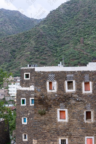 Ancient buildings built of stones, with a group of windows surrounded by white paint, in the middle of the Rijal Almaa Heritage Village, while the sky looks cloudy during the day