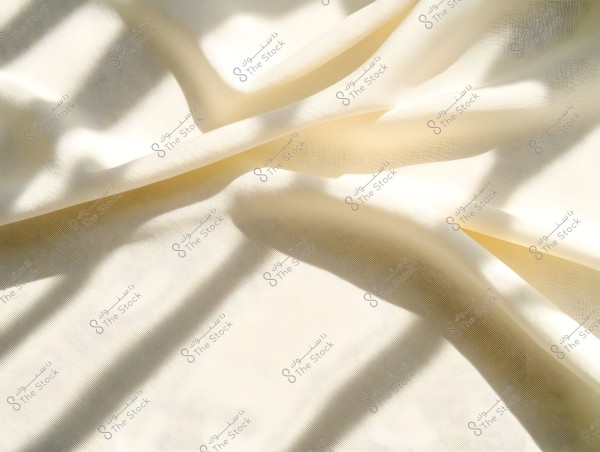 Image of a soft white fabric illuminated by sunlight, with folds and shadows adding depth and texture to the image. The light and shadows create an appealing pattern across the surface.