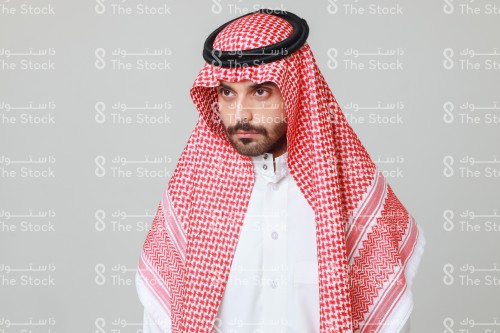 شاب سعودي يرتدي الزي السعودي التقليدي ينظر بتركيز و تمعن, رجل سعودي متعجب من أمر ما