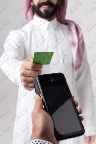 Portrait of a Saudi man holding a card and making automatic payments on a white background