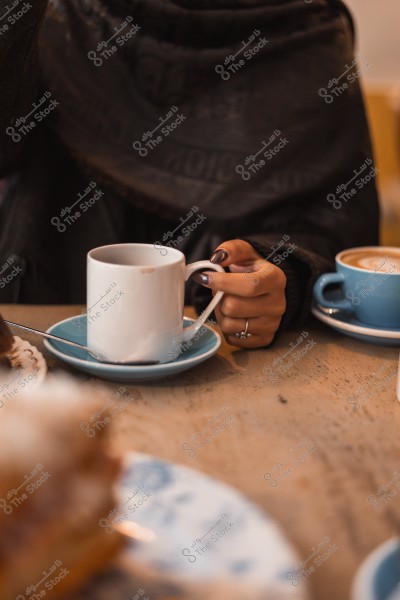 A woman holding a cup of coffee at a café table, with another cup visible on the side.