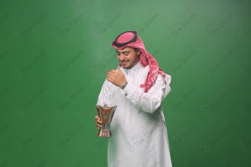 رجل سعودي يرتدي الزي التقليدي على خلفية خضراء ، التطيب بالبخور والعود ، استخدام خشب العود في المناسبات والأعياد.