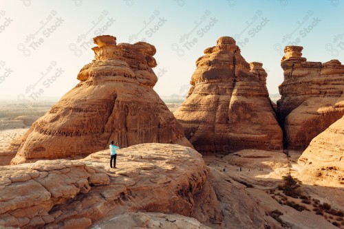 لقطة لسلسلة من الجبال في العلا، شخص يقوم بالتقاط صورة لجبال العلا، سماء صافية.