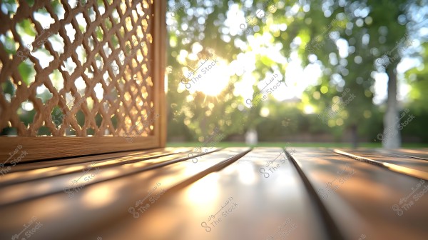 An image depicting an outdoor natural scene where sunlight shines through an intricately patterned wooden lattice. The wood is polished with a warm golden hue, beautifully reflecting the sunlight. In the background, there is a blurred view of grass and trees.