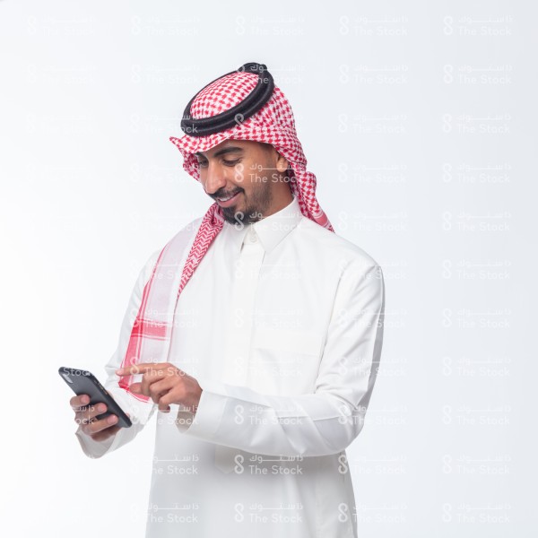 رجل سعودي يرتدي الزي السعودي ويستعمل الجوال مع خلفية بيضاء