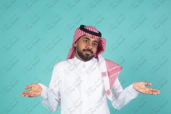 شاب سعودي على خلفية تركوازيه يعمل اشارات بيده ,تبدوا على ملامحه التعجب والاستغراب, ثوب و شماغ