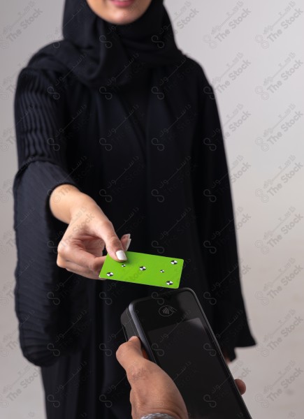 Portrait of a Saudi woman holding a card and making automatic payments on a white background