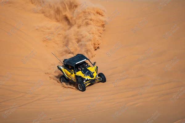 A yellow off-road vehicle speeds across sandy dunes in the desert. Sand is flying behind the vehicle as it moves forward, highlighting the dynamic motion of dune driving.