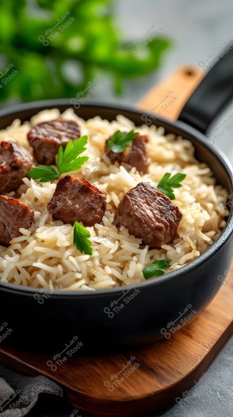 A dish of cooked white rice garnished with grilled meat pieces and green parsley leaves, placed in a black bowl on a wooden board. Green plant leaves are visible in the background.
