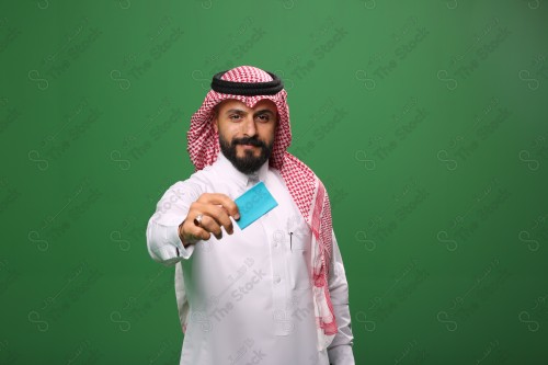 رجل سعودي على خلفية خضراء مبتسم يحمل بطاقة الصراف جاهز للتسوق