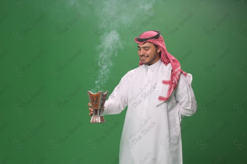 رجل سعودي يرتدي الزي التقليدي على خلفية خضراء ، التطيب بالبخور والعود ، استخدام خشب العود في المناسبات والأعياد.