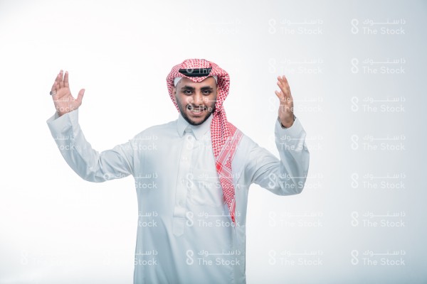 بورتريه رجل سعودي يرتدي الثوب ويقف أمام خلفية بيضاء ، مبتسم ،  يتفاعل بإشارات تعبيرية بيديه ، تعابير الفرح