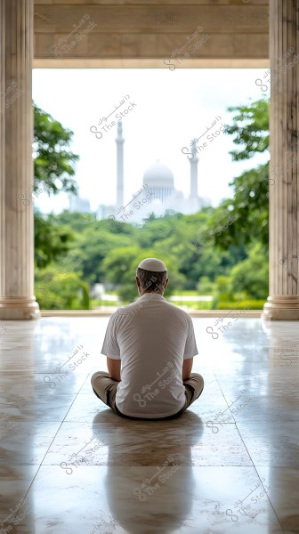 A man wearing a white cap and white shirt sits on a marble floor in a portico, overlooking a green landscape with a large mosque in the background. The scene is framed by marble columns and a clear sky.