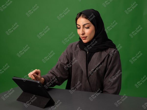امرأة ترتدي الحجاب تستخدام جهازًا لوحيًا أمام خلفية خضراء.