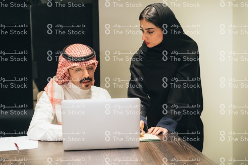 اجتماع عمل بين موظف سعودي يرتدي الثوب وموظفة سعودية ترتدي العباءة في قاعة الاجتماعات