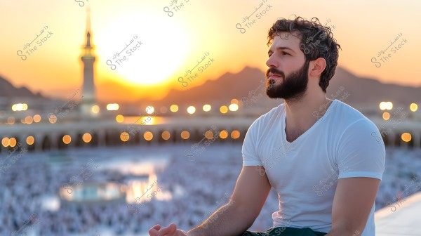Image of a man sitting wearing a white shirt in a public place, likely in Saudi Arabia, with a view of a minaret behind him and a sunset, along with a lit fence in the background. The golden lighting creates a calm and distinct atmosphere.