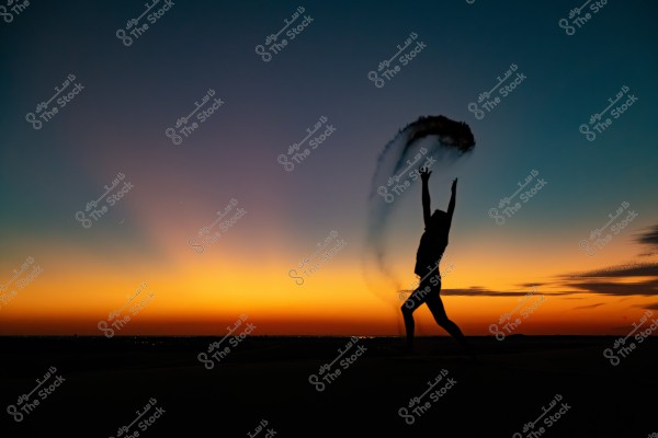 Image of a person jumping on sand at sunset, with a sky transitioning in color from blue to orange. The person appears as a silhouette, stretching their arms upward while tossing sand, forming an attractive arc in the air. City lights or distant lights are visible on the horizon.