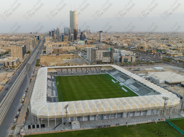 An aerial shot of Al-Shabab Club stadium, with the towers of Riyadh city behind it, football fields, and sports fields