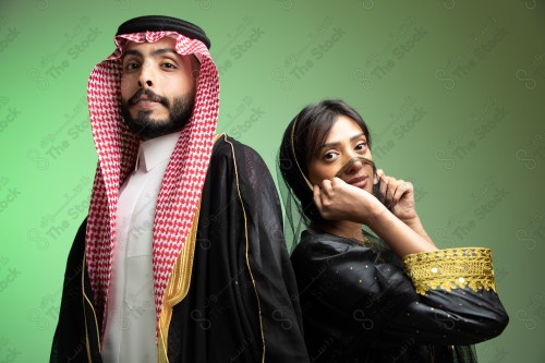 رجل سعودي يرتدي الزي السعودي وامرأه سعودية ترتدي المخنق والزي السعودي التقليدي الشعبي للمناسبات والإحتفالات الوطنية على خلفية خضراء