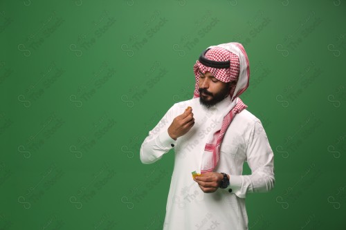 بورتريه رجل سعودي يرتدي الزي السعودي التقليدي يتناول الحلوى