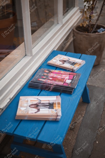 Colorful magazines placed on a blue wooden table in front of a display window.