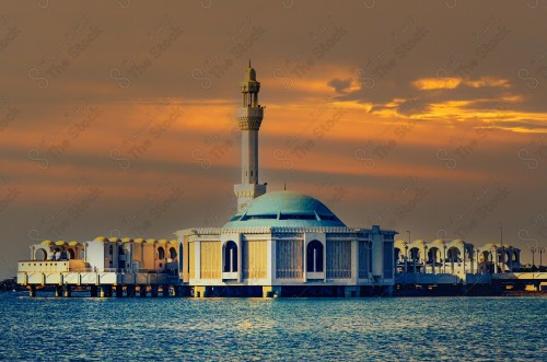 A shot of the Al-Rahma Mosque surrounded by palm trees on Jeddah Corniche, showing the orange overcast sky at sunset.