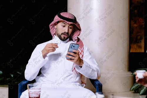 شاب سعودي يرتدي الزي السعودي التقليدي يستخدم جواله في المقهى