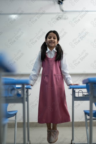 A Saudi student wears a school uniform and does different interactions and shows the tables in the classroom