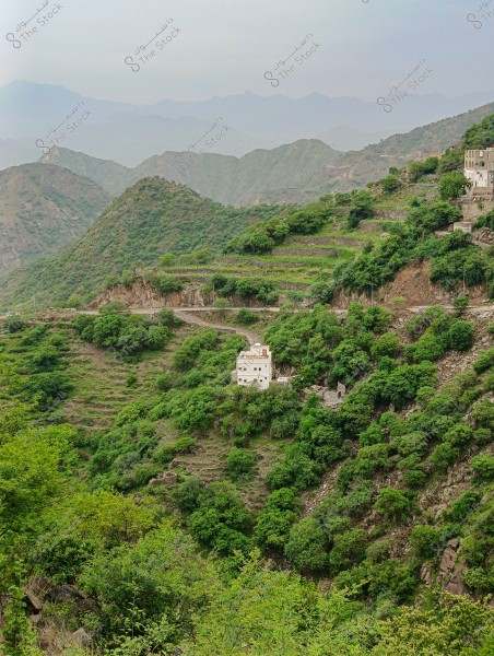 The image depicts a natural landscape of a mountain covered with dense green vegetation and trees, with scattered houses built on the terraced slopes of the mountain. The weather appears cloudy and calm, with hills and mountains in the background extending to the horizon.