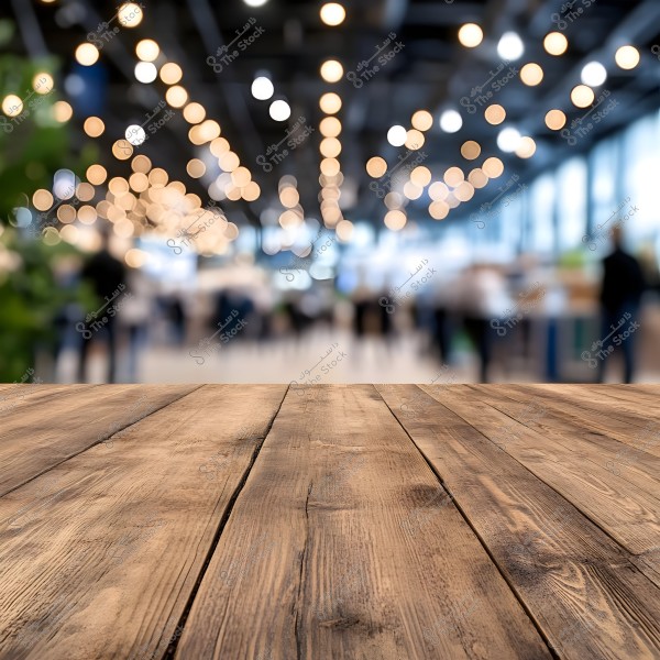 A wooden tabletop in the foreground with a blurred background of a modern shopping center, featuring bright lights and people walking around.