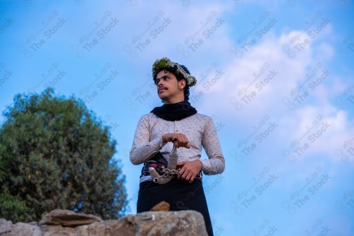 A Saudi man wearing a traditional dress at the top of the mountain and behind him clouds appear in Jizan