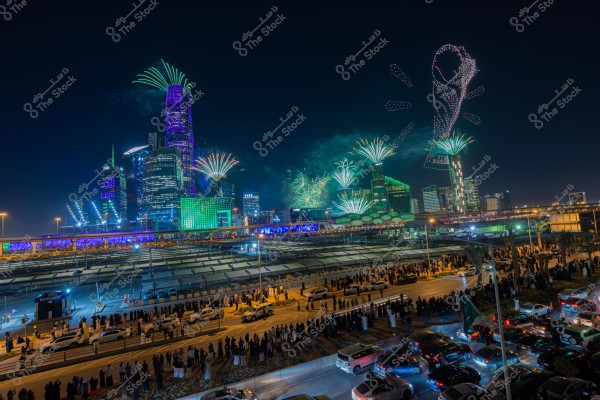 A nighttime celebration in a modern city with skyscrapers illuminated in green and fireworks lighting up the sky. The lights are arranged to form a cup, symbolizing a major sports event. A large crowd of people is gathered to observe the spectacle, with cars lined up on the road. The atmosphere is one of grandeur and excitement.