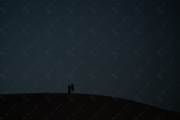 A shot of a man and a woman on top of a sandy dunes in the Empty Quarter desert, a stunning view of the stars and sand dunes