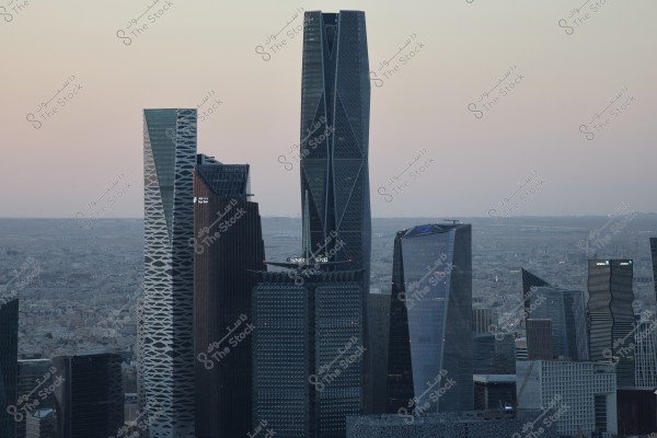The image shows a view of the financial district in Riyadh, Saudi Arabia. The scene includes tall skyscrapers such as the King Tower, Fairmont Hotel, Riyadh Bank Tower, and the Capital Market Authority Tower. The skyline in the background at sunset gives a serene feeling to the modern and advanced architectural horizon.