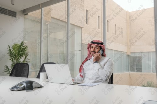 A Saudi man wearing the Saudi thobe sits in the meeting room and uses the mobile device