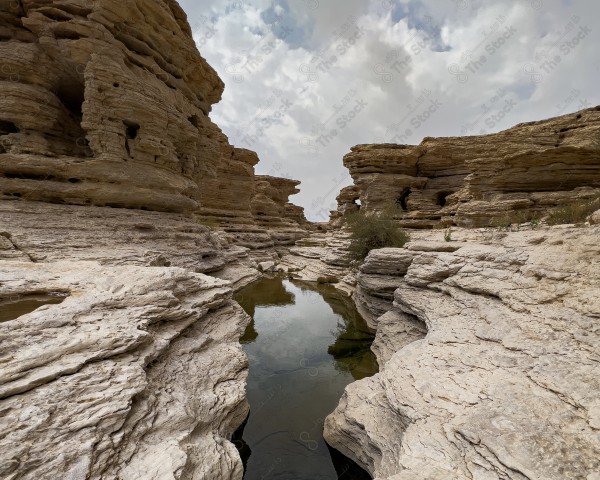 لقطة لاحد الاودية لسلسلة جبال طويق في منطقة نجد وتظهر السماء غائمة ، سلسلة من الجبال الصخرية ، تكوينات صخرية.