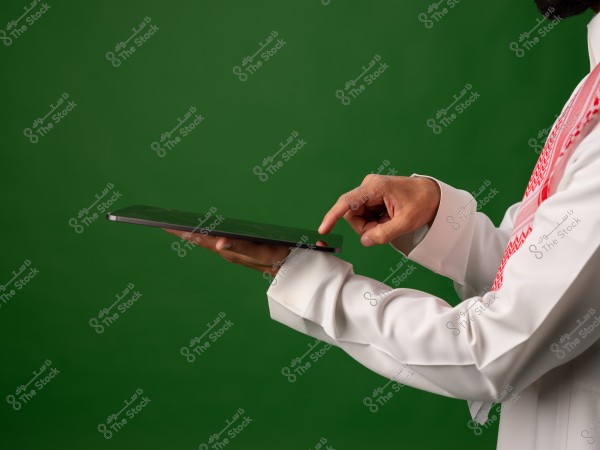 يُظهر الصورة شخصًا يرتدي الثوب والغترة التقليدية وهو يستخدم جهازًا لوحيًا بإصبعه مقدمةً على خلفية خضراء.
   
-