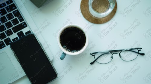 A shot of a work table with a cup of coffee, hot drinks, glasses, a glass of water, and a phone.