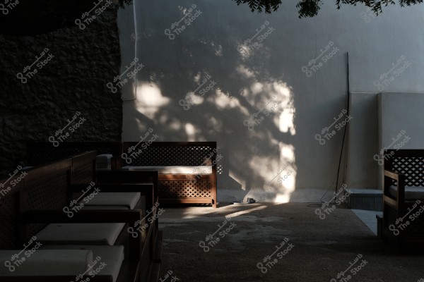 Outdoor seating with wooden furniture and tree shadows on a white wall.
