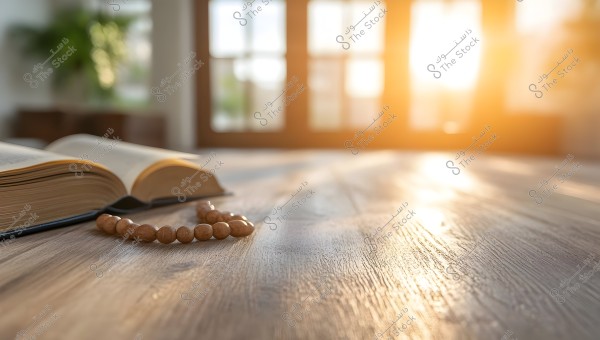 The image shows an open book placed on a wooden table with a wooden prayer bead beside it. Bright sunlight is streaming in through a large window in the background, creating a warm and naturally lit atmosphere in the room.