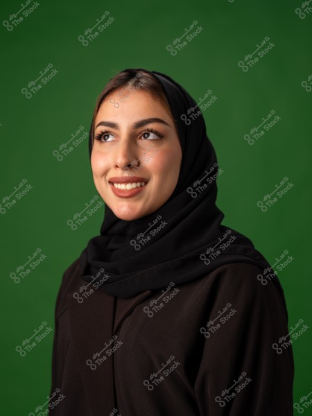 امرأة ترتدي حجابًا أسود تقف أمام خلفية خضراء.