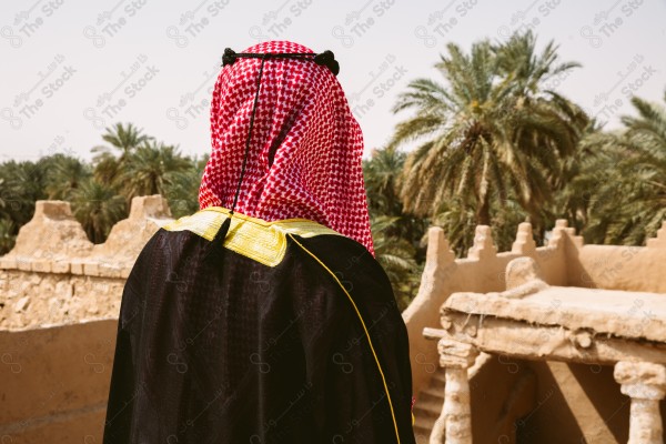 لقطة لرجل سعودي يرتدي الزي التراثي الشعبي في يوم التأسيس يقف فوق مبنى طيني, الزي التراثي, يوم التأسيس, مباني أثريه قديمه.